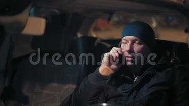 特写镜头，男人在电话上说话，晚上坐在停车场的车轮上
